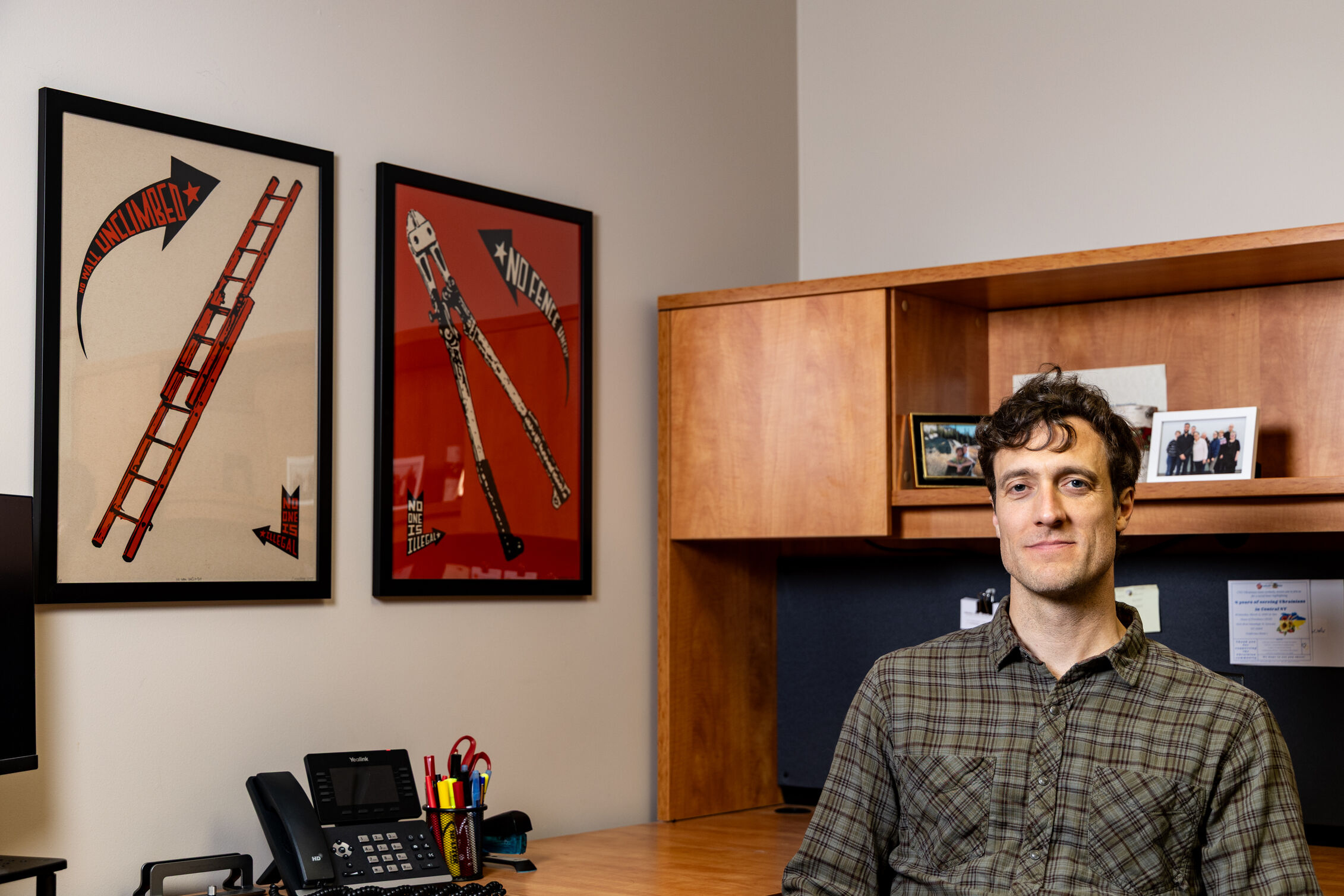 Benjamin Vernon sits in his wooden cubicle in a green plaid shirt.