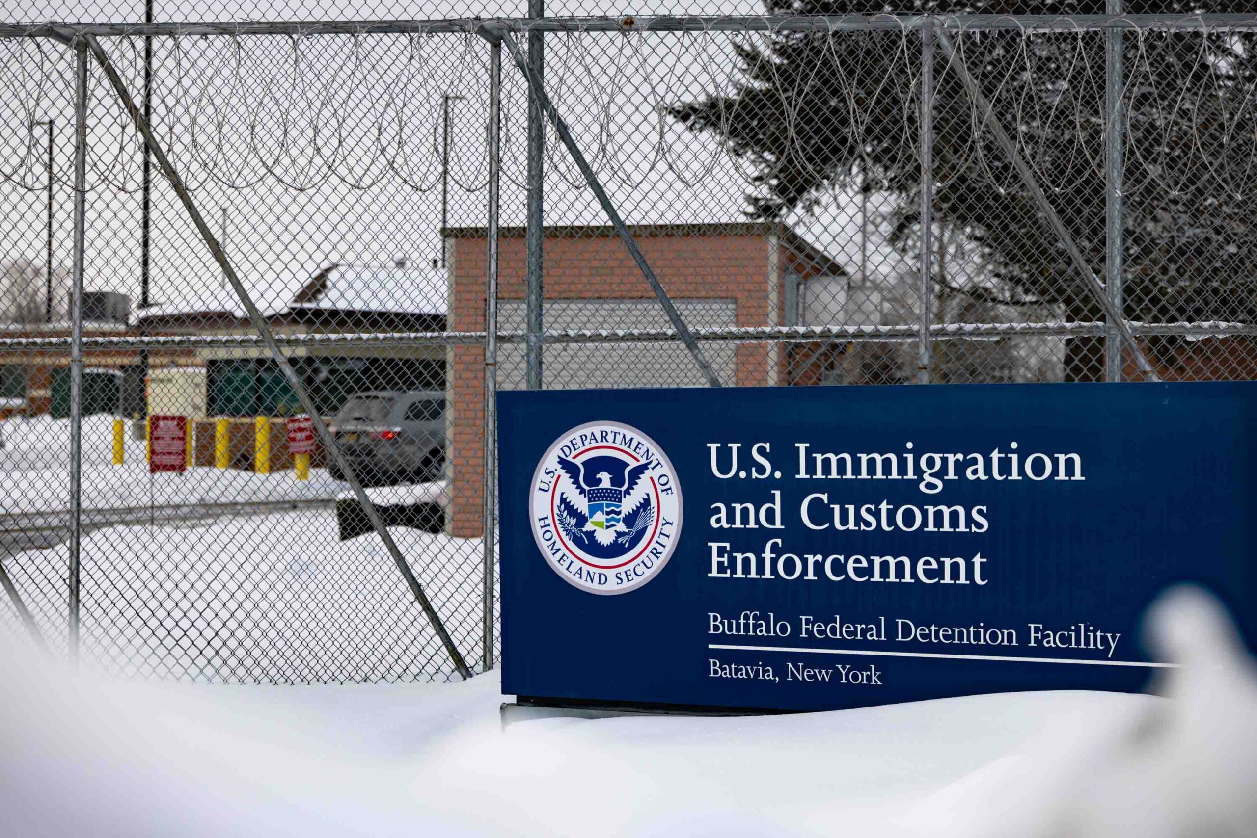 Outside Batavia's ICE Detention Center sits a blue sign in the snow that reads "U.S. Immigration and Customs Enforcement"