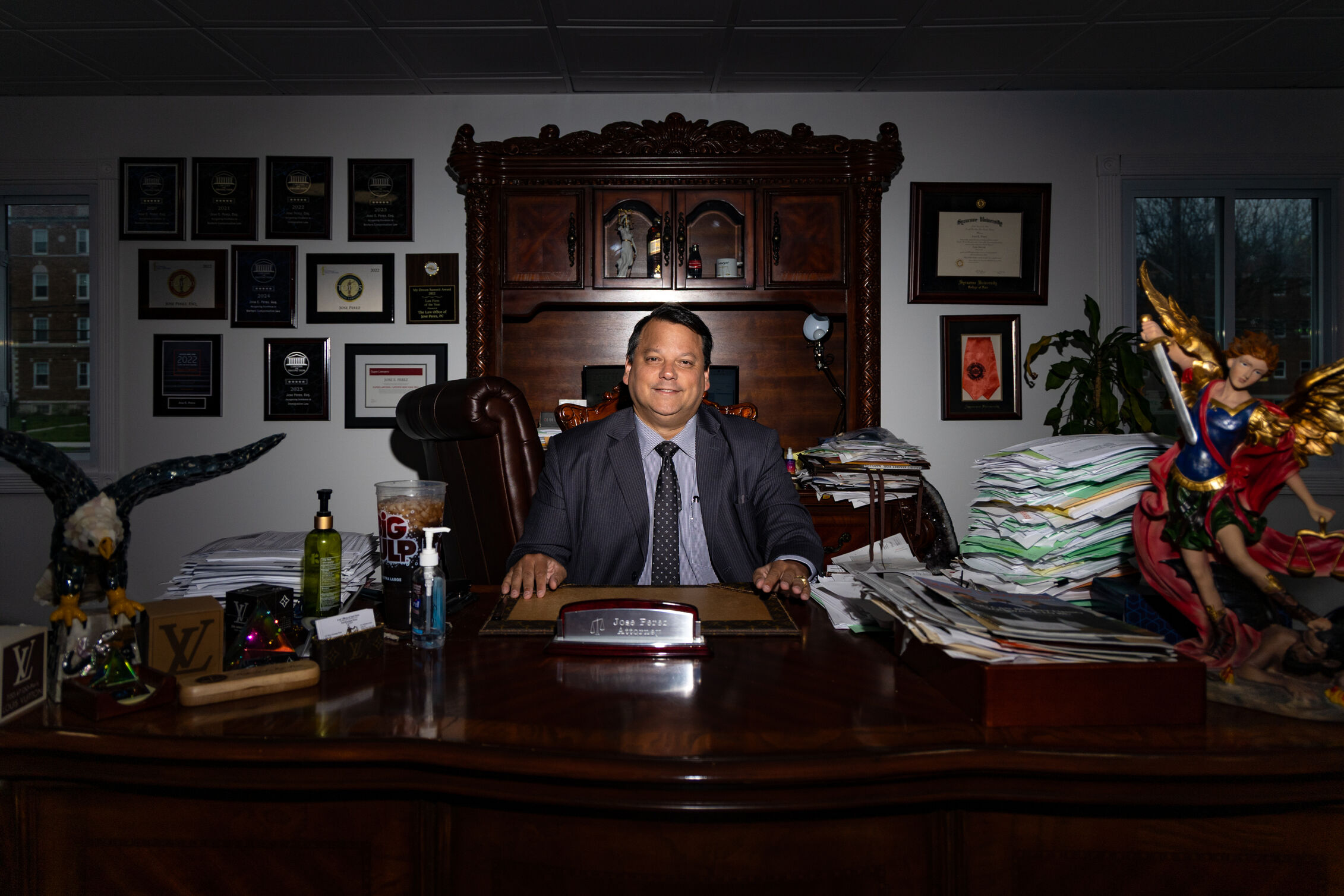 Jose Perez sits at his desk surrounded by stacks of papers.