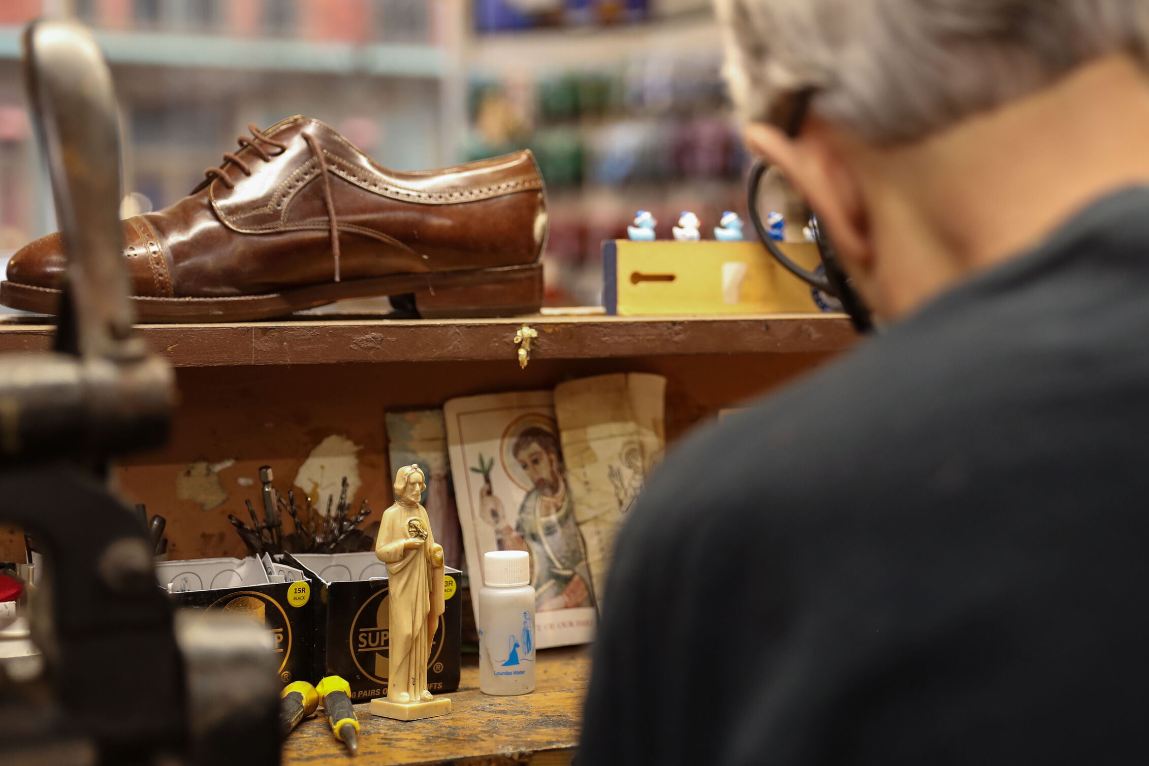 Ralph Rotella in his shoe shop where at his desk sits a leather shoe and a small figure of Jesus.