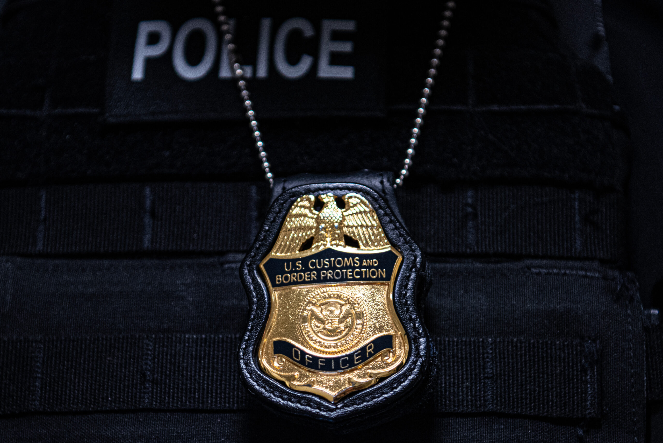 A close up of a badge hanging around the neck of an officer that reads "U.S. Customs and Border Protection Officer."