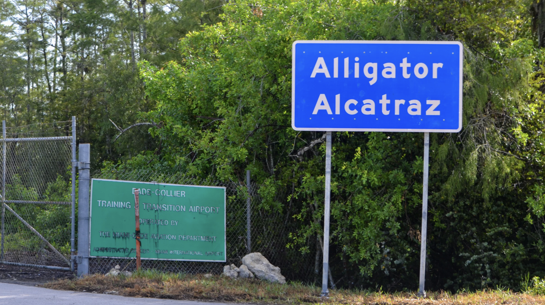 The former "Dade-Collier Transition and Training Airport" sign lies disregarded next to the newly-built "Alligator Alcatraz" sign on July 12, 2025. After it was built in early June, the site quickly became a hub for Florida's deportation efforts.
