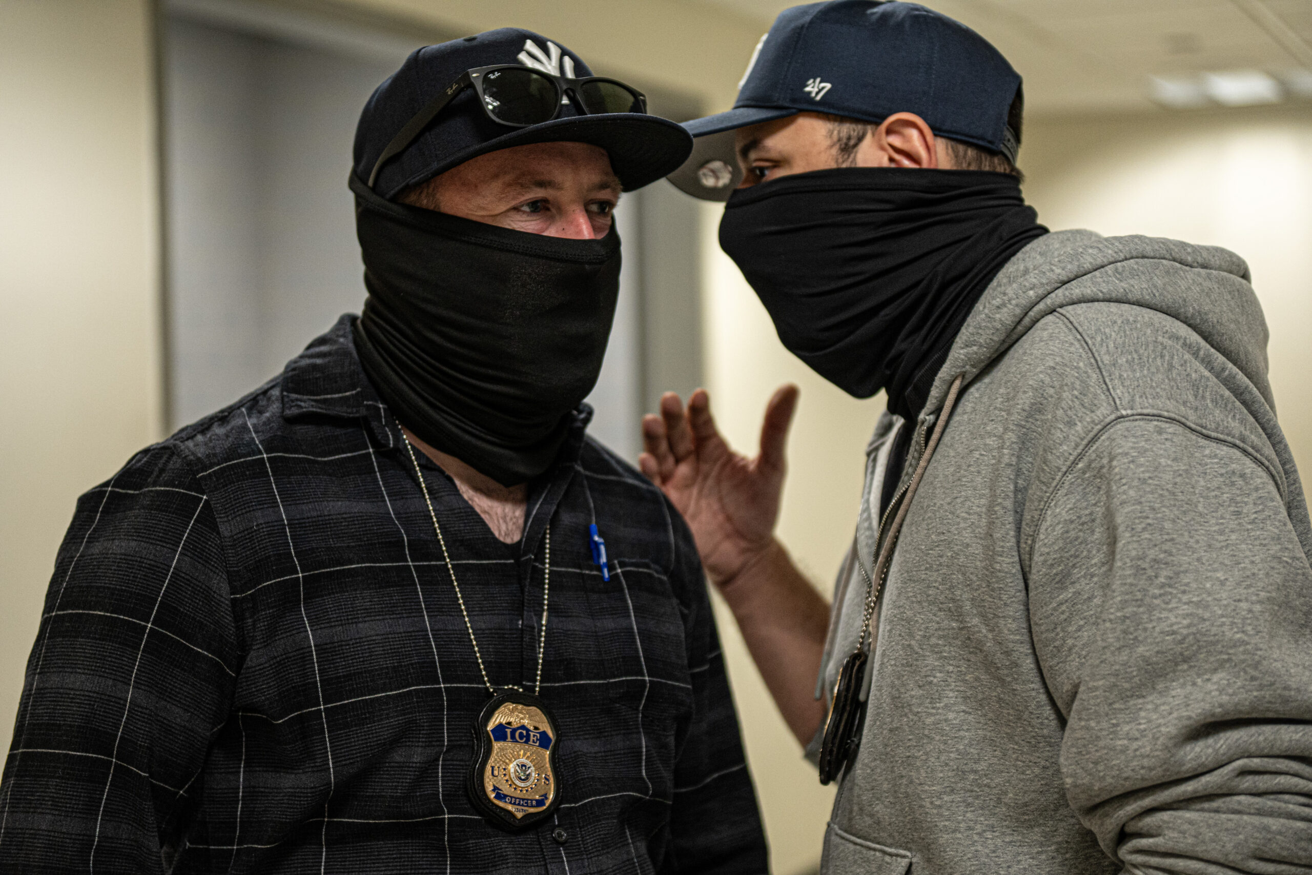 Two ICE agents confer quietly about a person who arrived by elevator on the 14th floor of the Jacob K. Javits Federal Building in New York on March 9, 2026. The agents' interest appeared to be prompted by the person's appearance. Inside 26 Federal Plaza, federal agents sometimes speak candidly in front of journalists. "Everybody asks me how's life going and I tell them I'm living the dream, but it's a lie — I'm living a nightmare," one agent said before being cut off by a colleague. "Let's start with the country," the second agent said.