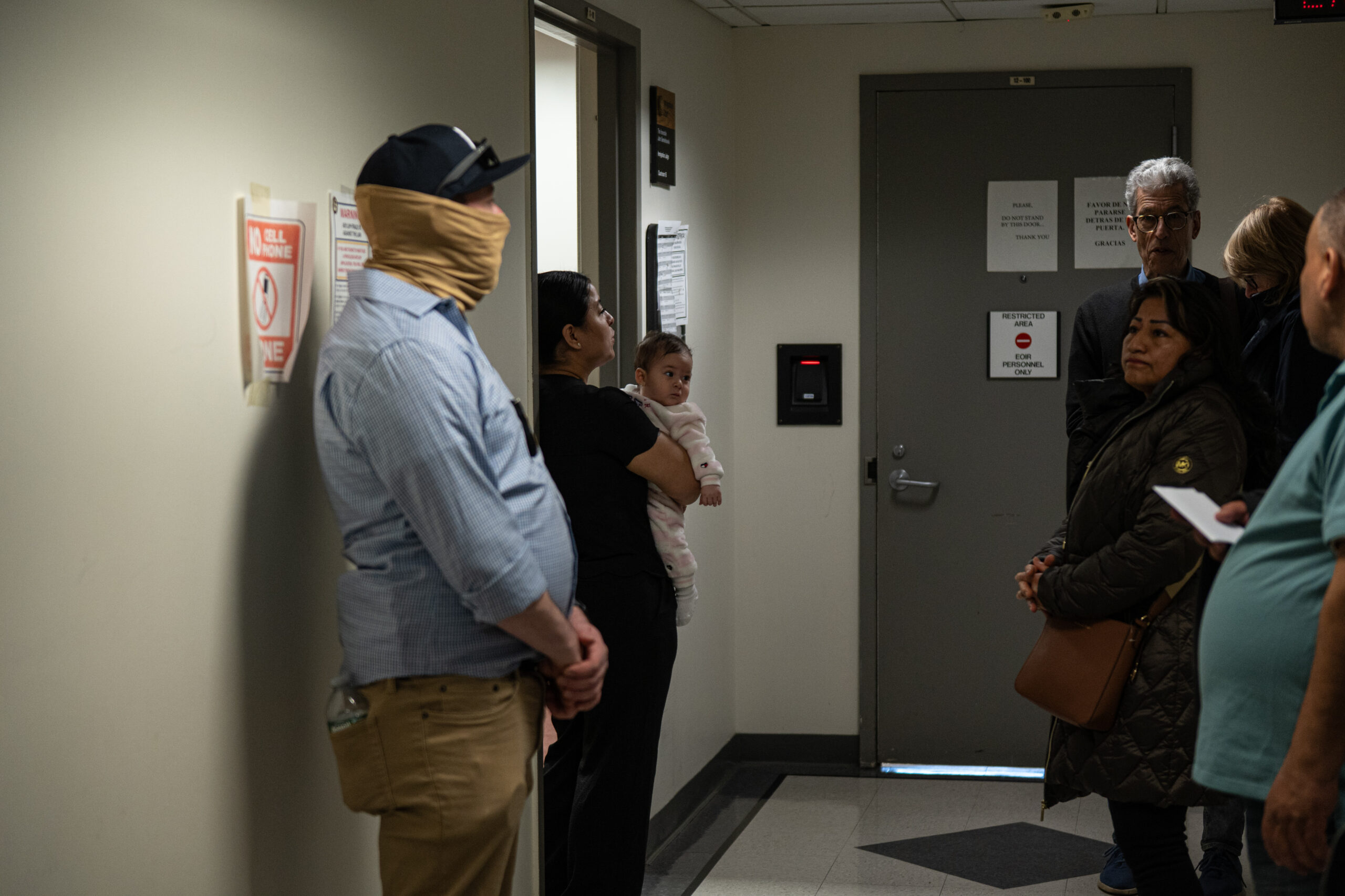 A mother holds her child while her husband attends an immigration check-in at 26 Federal Plaza in New York on March 11, 2026.